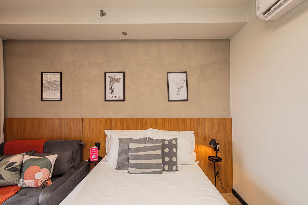 A hotel room with a bed, a wooden headboard, a nightstand with a lamp, and three framed maps on the wall.