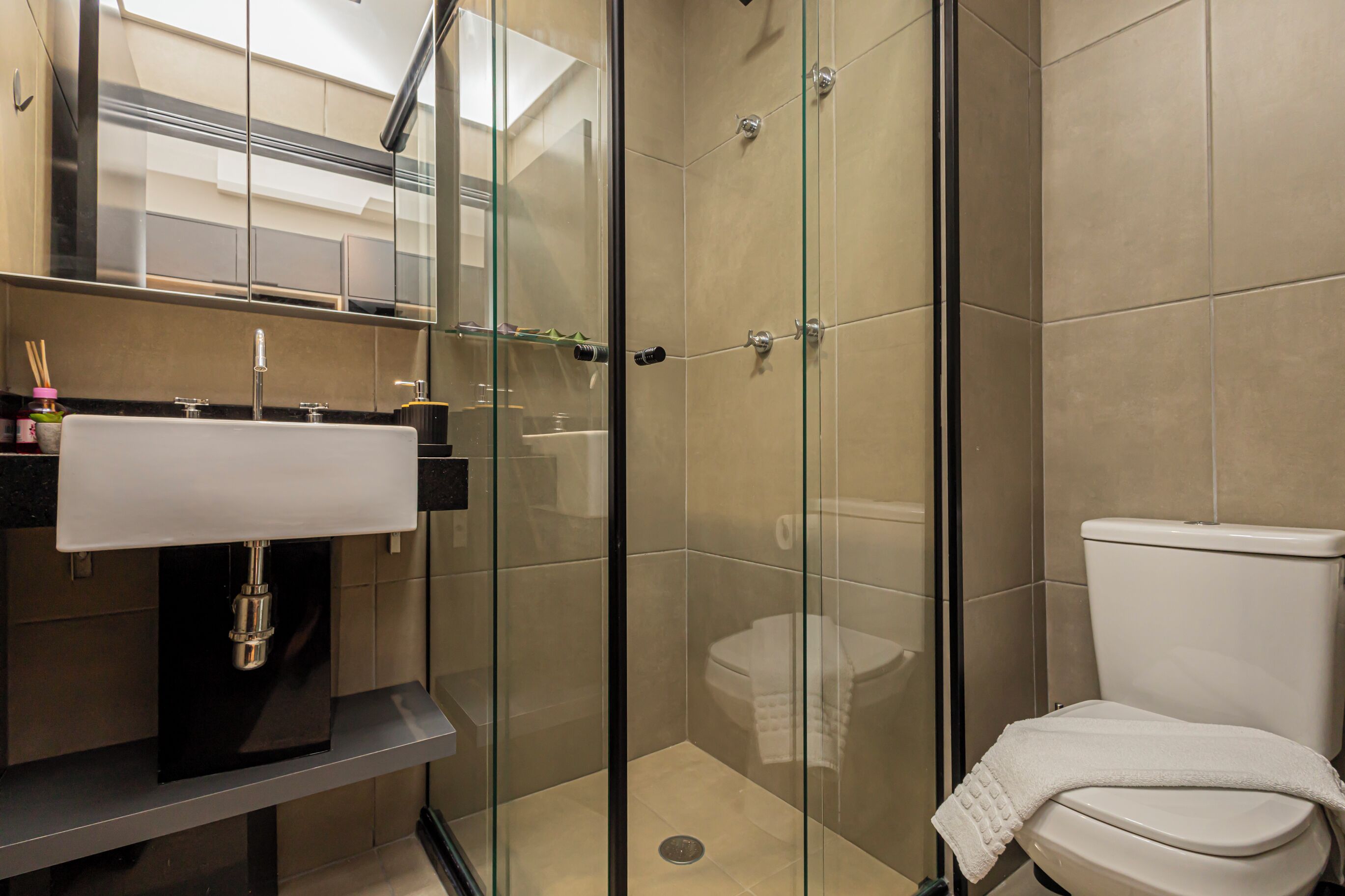 Un bany modern amb dutxa amb envàs de vidre, un lavabo blanc i un vàter.