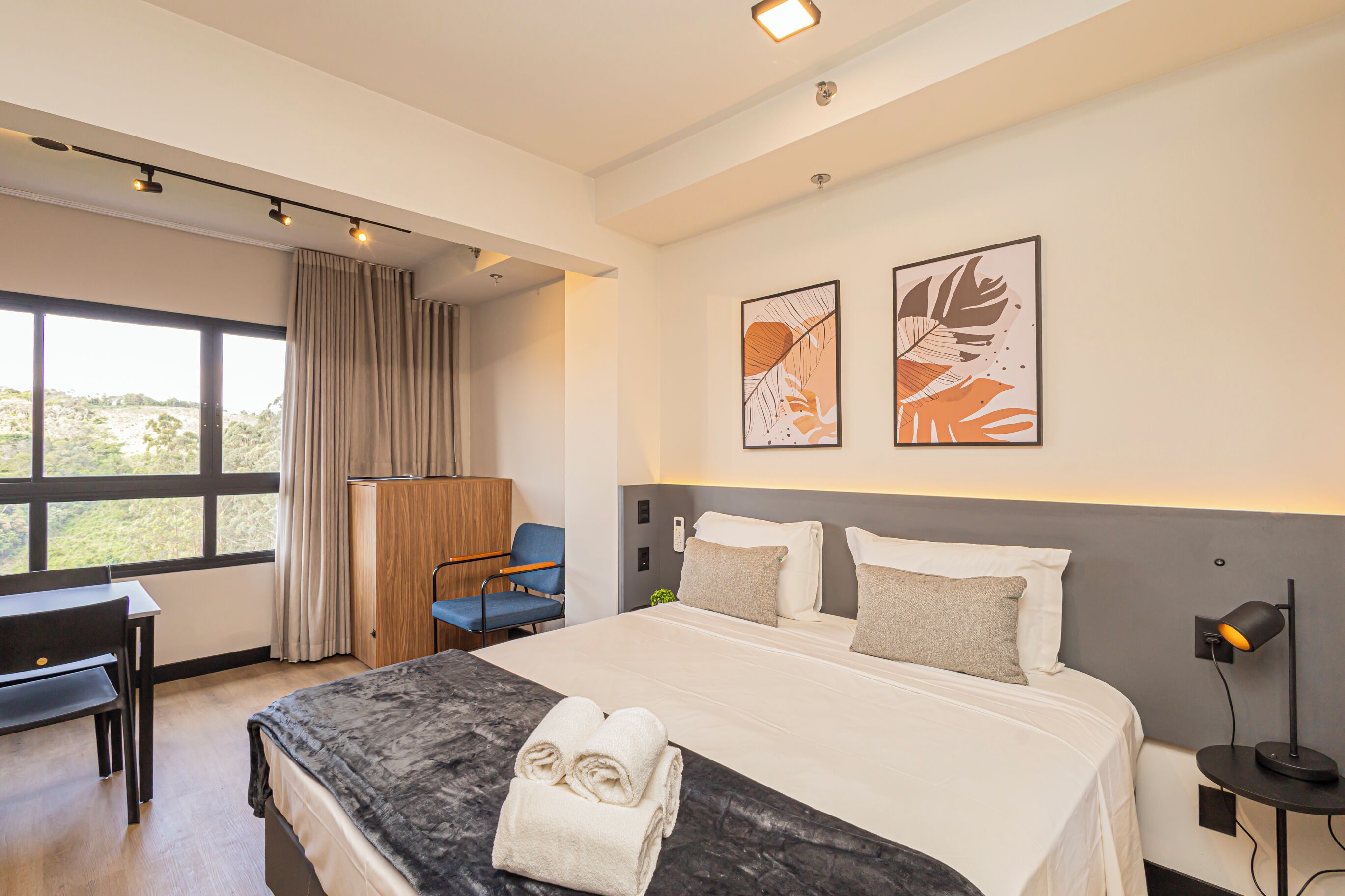 Una habitación de hotel moderna con una cama grande, un escritorio, una silla y obras de arte en la pared.