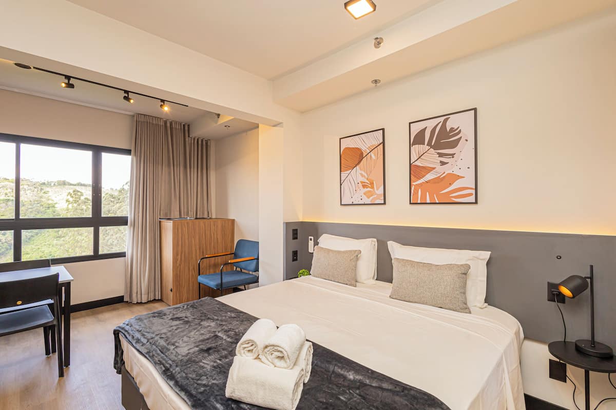 A modern hotel room with a large bed, a desk, a chair, and artwork on the wall.