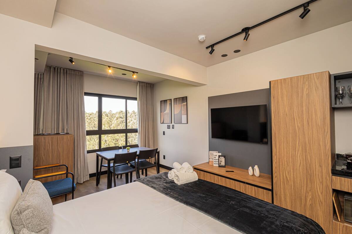 A modern hotel room with a bed, a desk, a TV, and a view of the outdoors.
