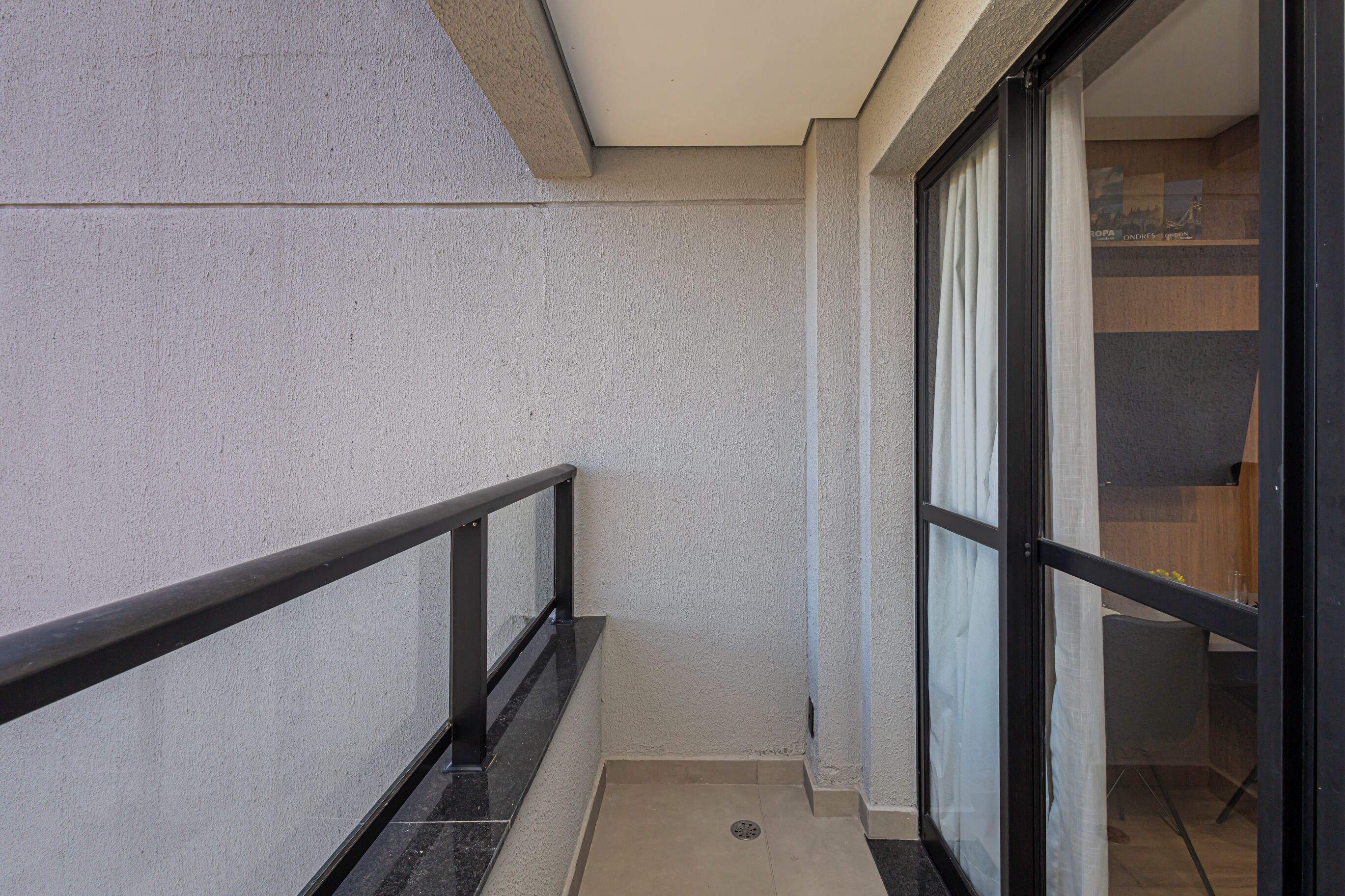 A narrow balcony with a black railing, a glass door, and a small indoor area with a table and chairs.