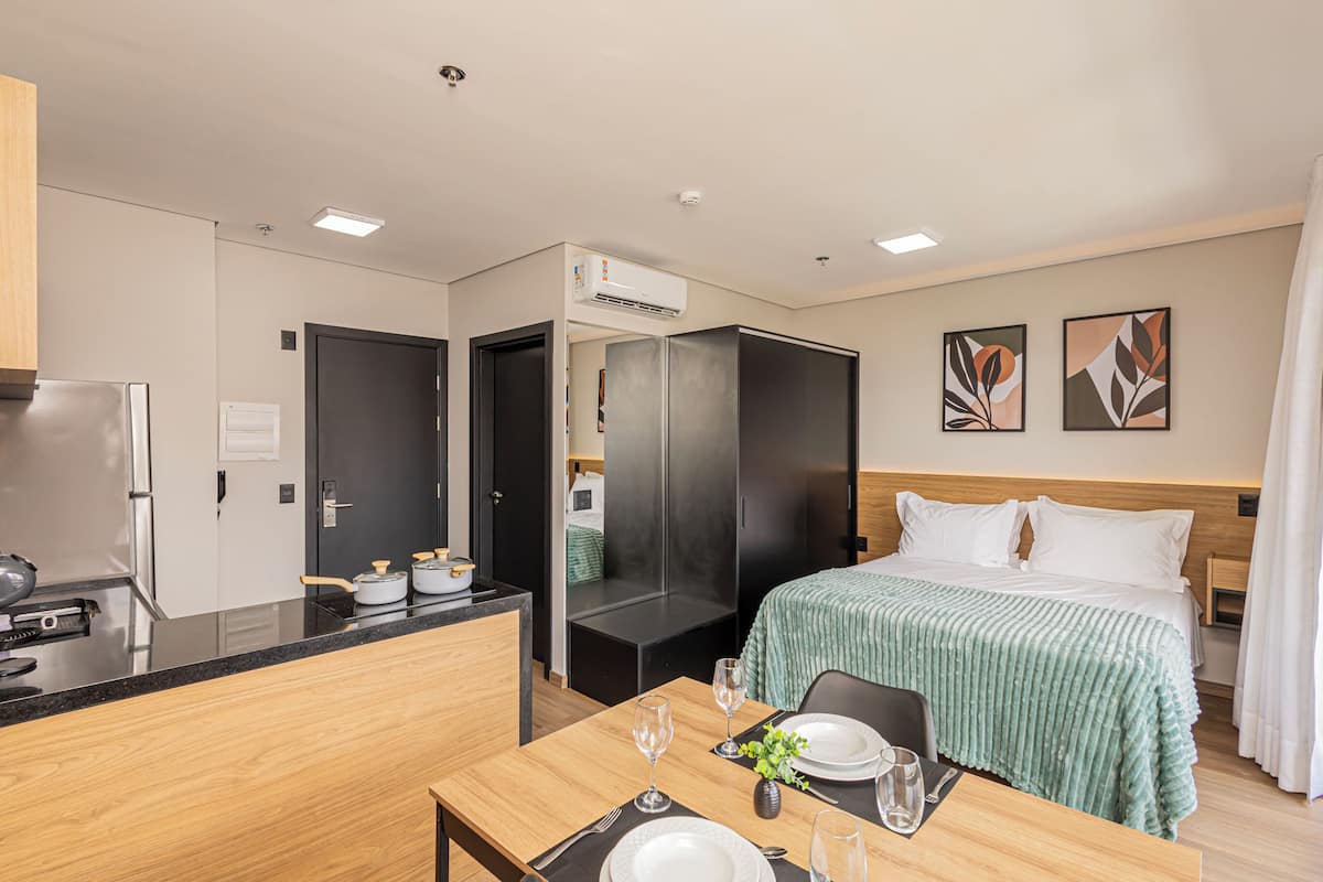 A hotel room with a bed, a dining table set for two, a kitchenette, and a wardrobe.