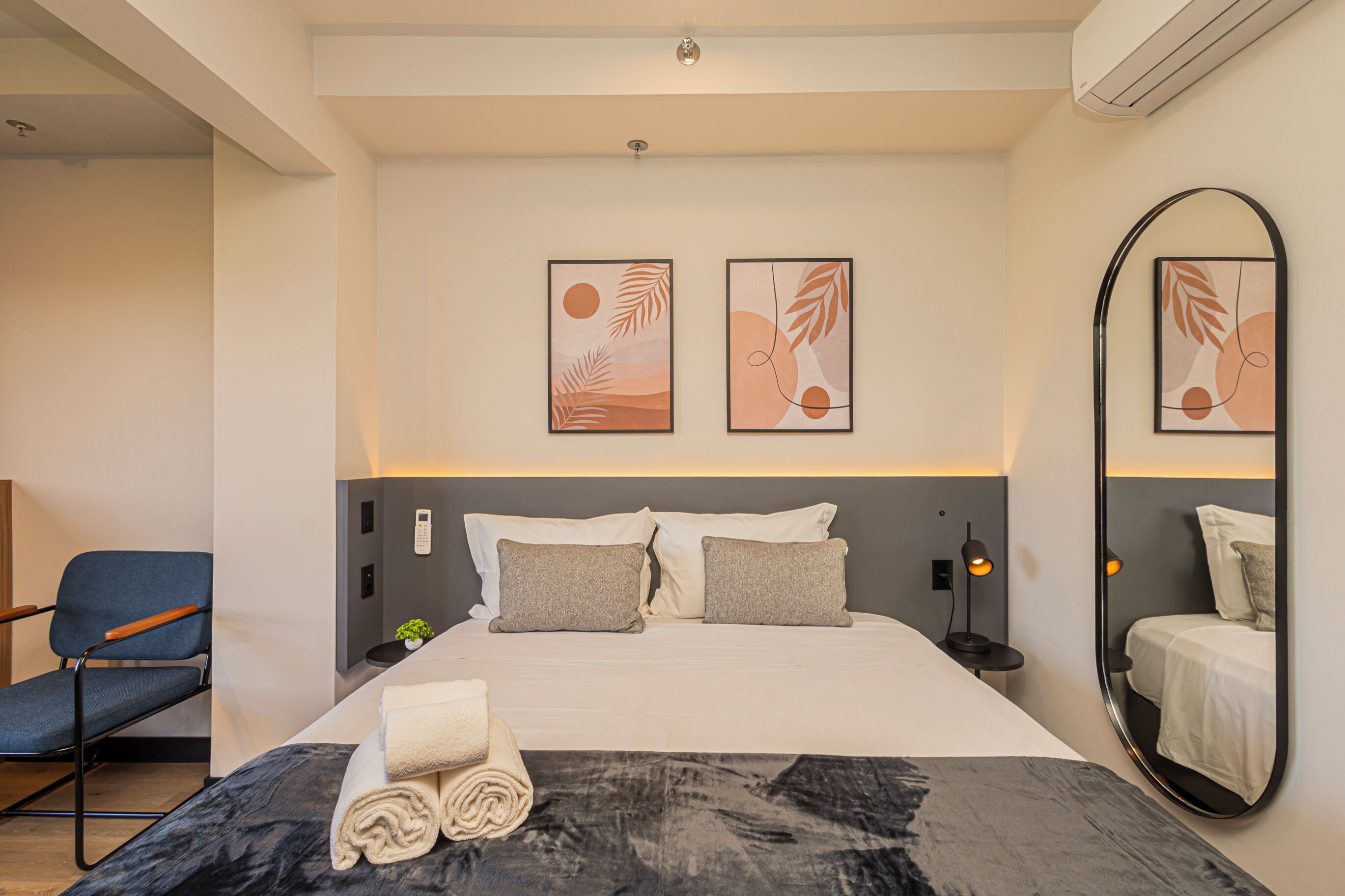Habitación de hotel con cama, una silla, un espejo instalado en la pared y dos cuadros enmarcados.