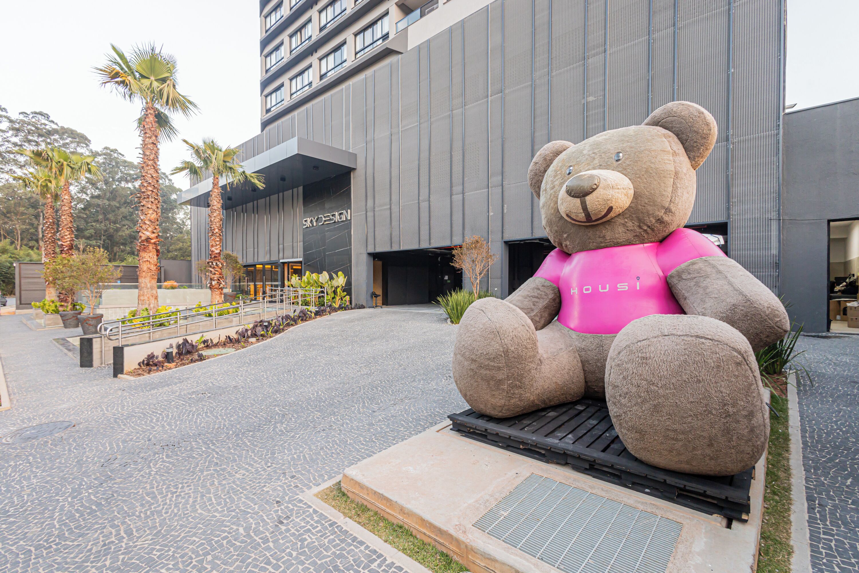 A large outdoor sculpture of a bear wearing a pink shirt, located in front of a modern building with a sign that reads "Skyline."