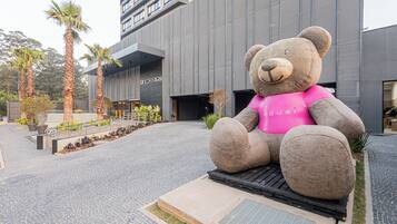 A large outdoor sculpture of a bear wearing a pink shirt, located in front of a modern building with a sign that reads "Skyline."