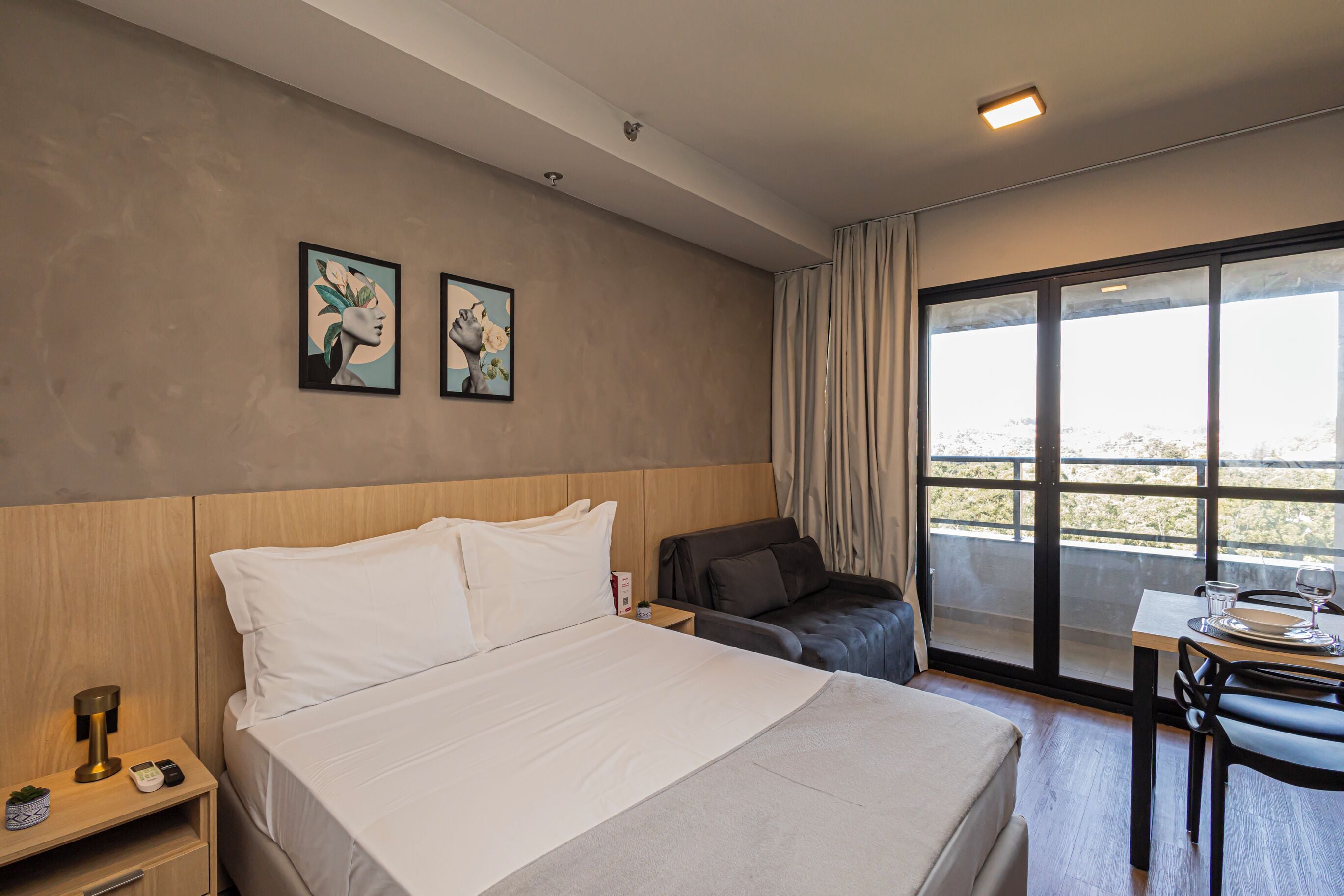 Una habitación de hotel con cama, un escritorio con silla, una ventana con cortinas y una obra de arte en la pared.