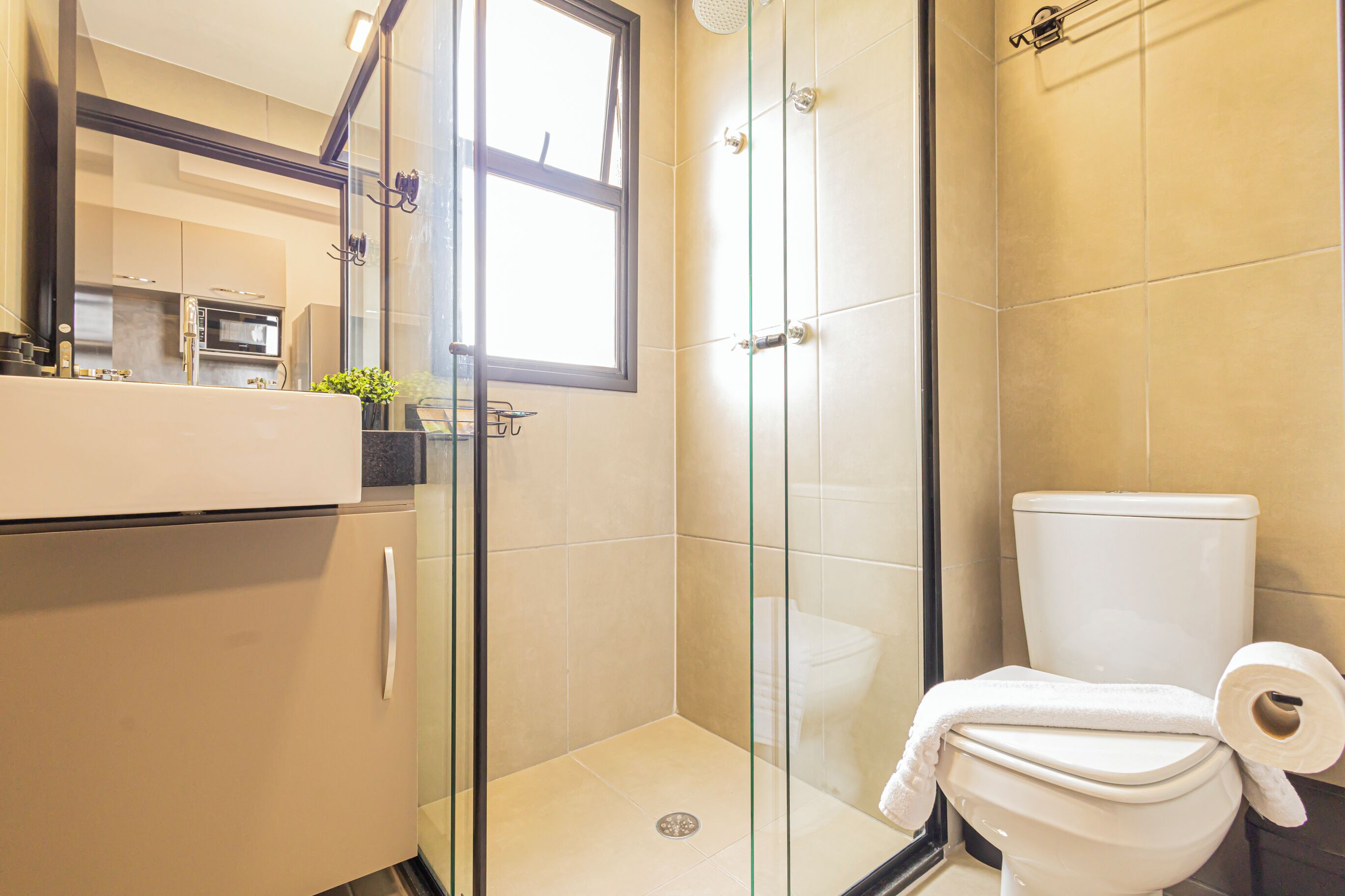 Un bany modern amb plat de dutxa envoltat de vidre, un vàter amb tovallola i un lavabo amb mirall a sobre.