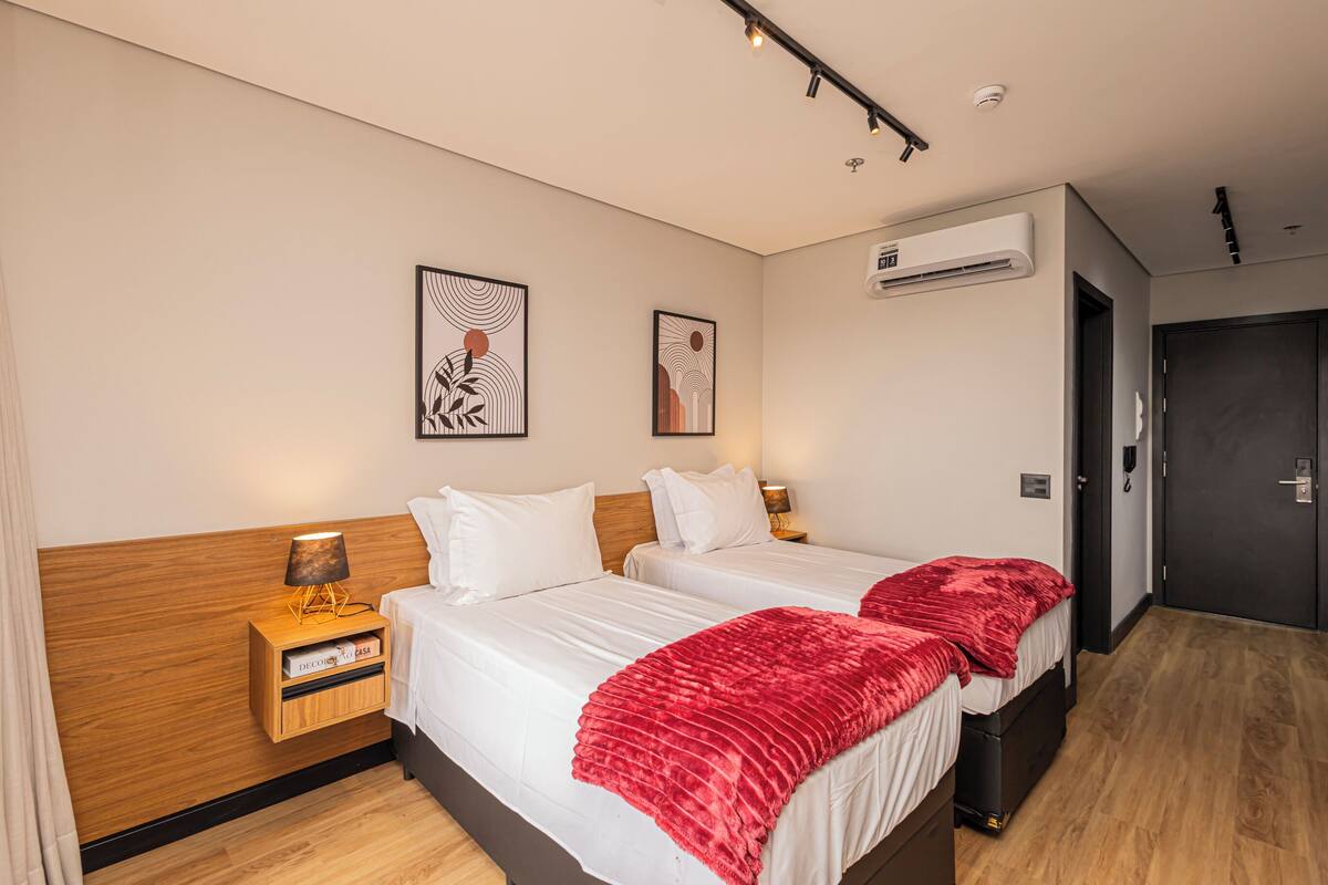 A hotel room with two beds, a wooden headboard, a nightstand with a lamp, and artwork on the wall.