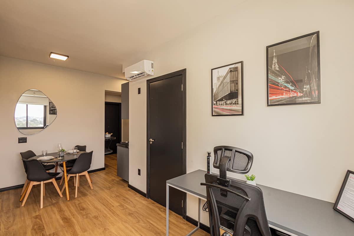 A modern hotel room with a dining area, a desk, and two framed pictures on the wall.