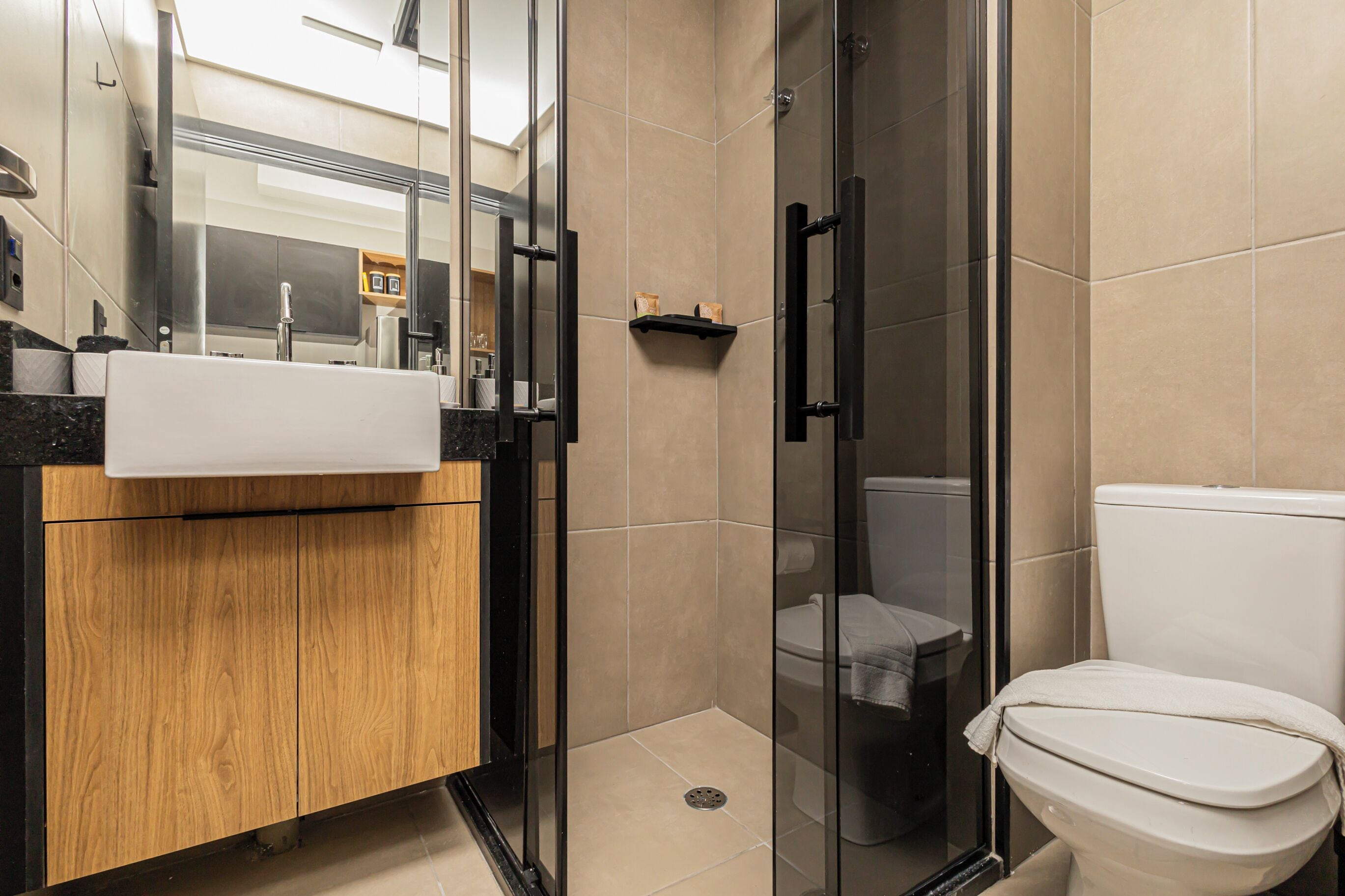 A modern bathroom with a glass shower enclosure, a wooden vanity, and a white toilet.