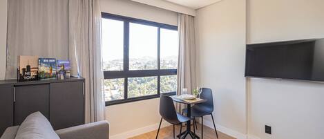 Una sala moderna con sofá, mesa de comedor y sillas, televisor de pantalla plana montado en la pared y ventana con vista a la ciudad.