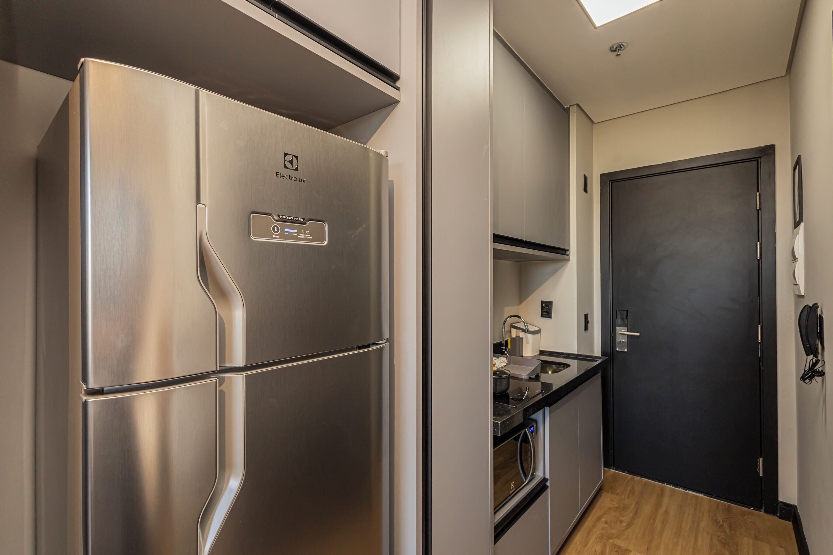 Una cocina moderna con un refrigerador de acero inoxidable, una puerta negra y piso de madera.