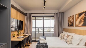 Ein modernes Hotelzimmer mit einem großen Bett, einem Schreibtisch mit Fernseher und einem Balkon mit Vorhängen.
