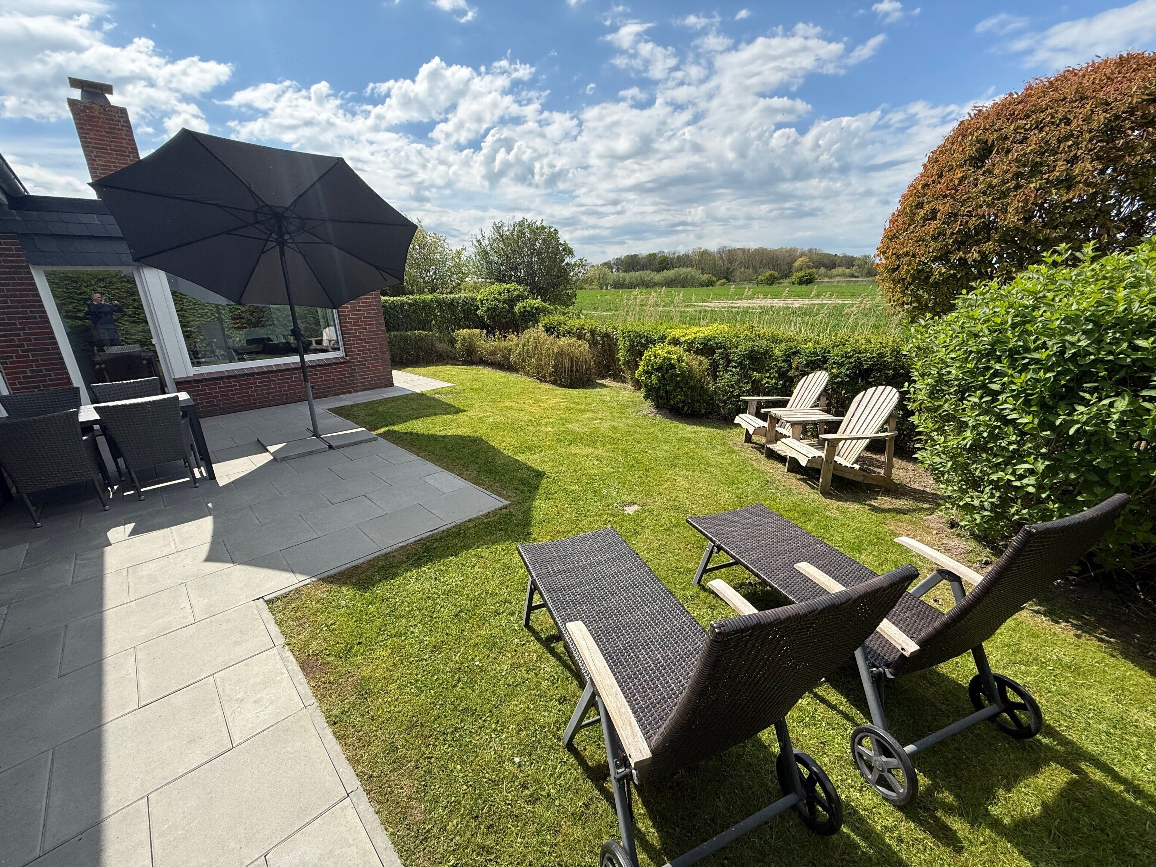 A patio area with outdoor furniture, a large umbrella, and a view of the countryside.