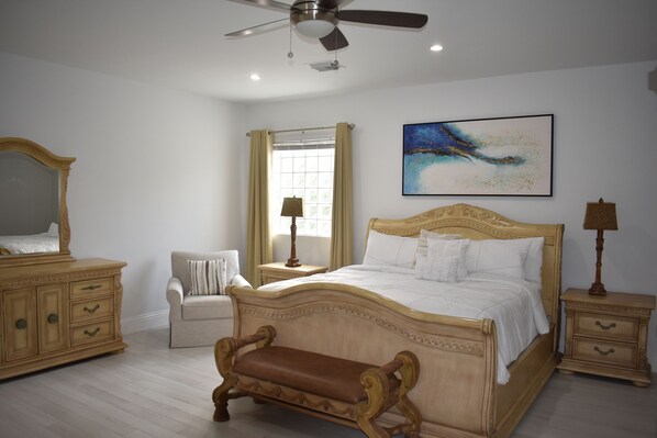 A bedroom with a large bed, a wooden bench, a dresser, a nightstand, and a ceiling fan.