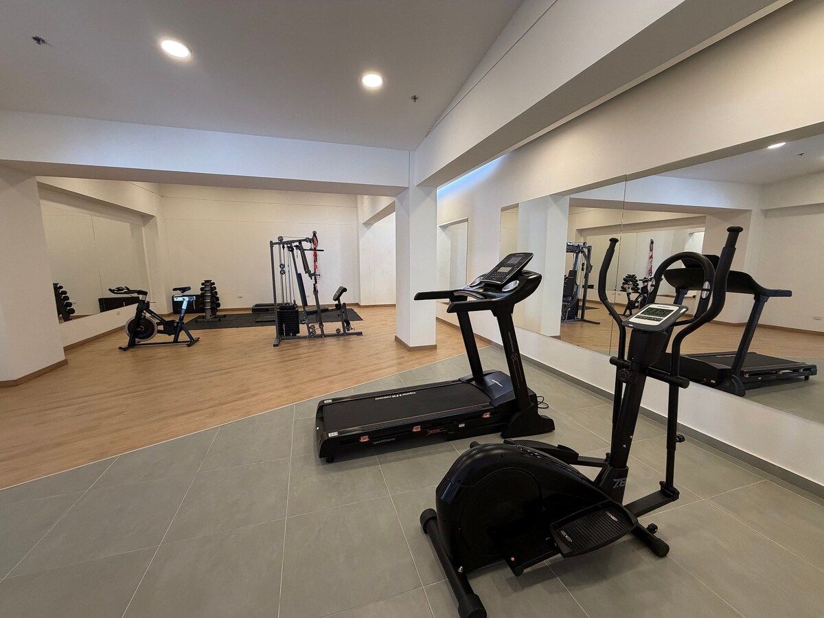 Un gimnasio con cintas de correr, elípticas y equipo de levantamiento de pesas.