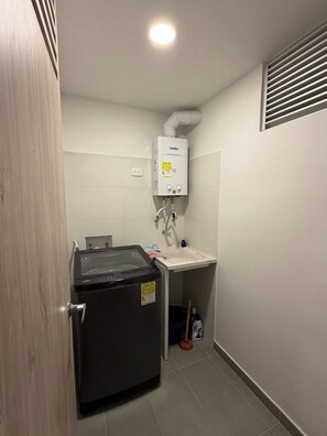 Une petite salle de bain équipée d’un lave-linge encastré, d’un lavabo et d’un radiateur.