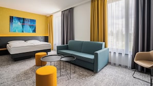 Een moderne hotelkamer met een bed, een slaapbank, twee kleine tafels en een stoel.