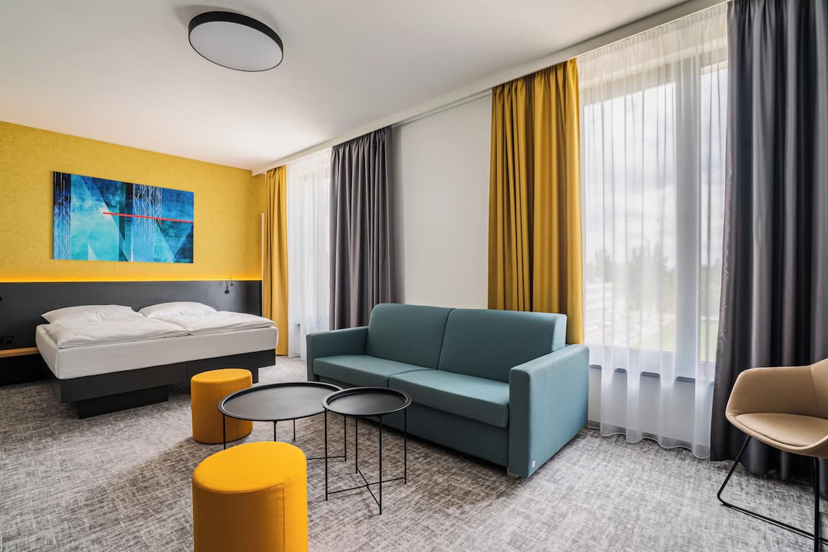 Een moderne hotelkamer met een bed, een slaapbank, twee kleine tafels en een stoel.