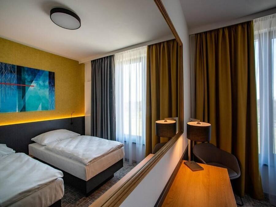 A hotel room with two beds, a desk, a chair, a large mirror, and a view of the city.