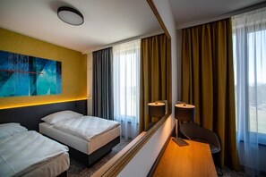 Une chambre d’hôtel avec deux lits, un bureau, une chaise, un grand miroir et une vue sur la ville.