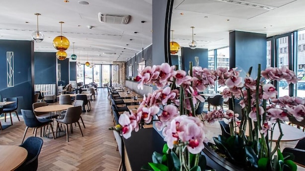 Een modern restaurant met een lange toonbank, houten vloer en grote ramen.