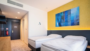 Een hotelkamer met twee eenpersoonsbedden, een houten tafel, een brandblusser en een groot abstract schilderij aan de muur.