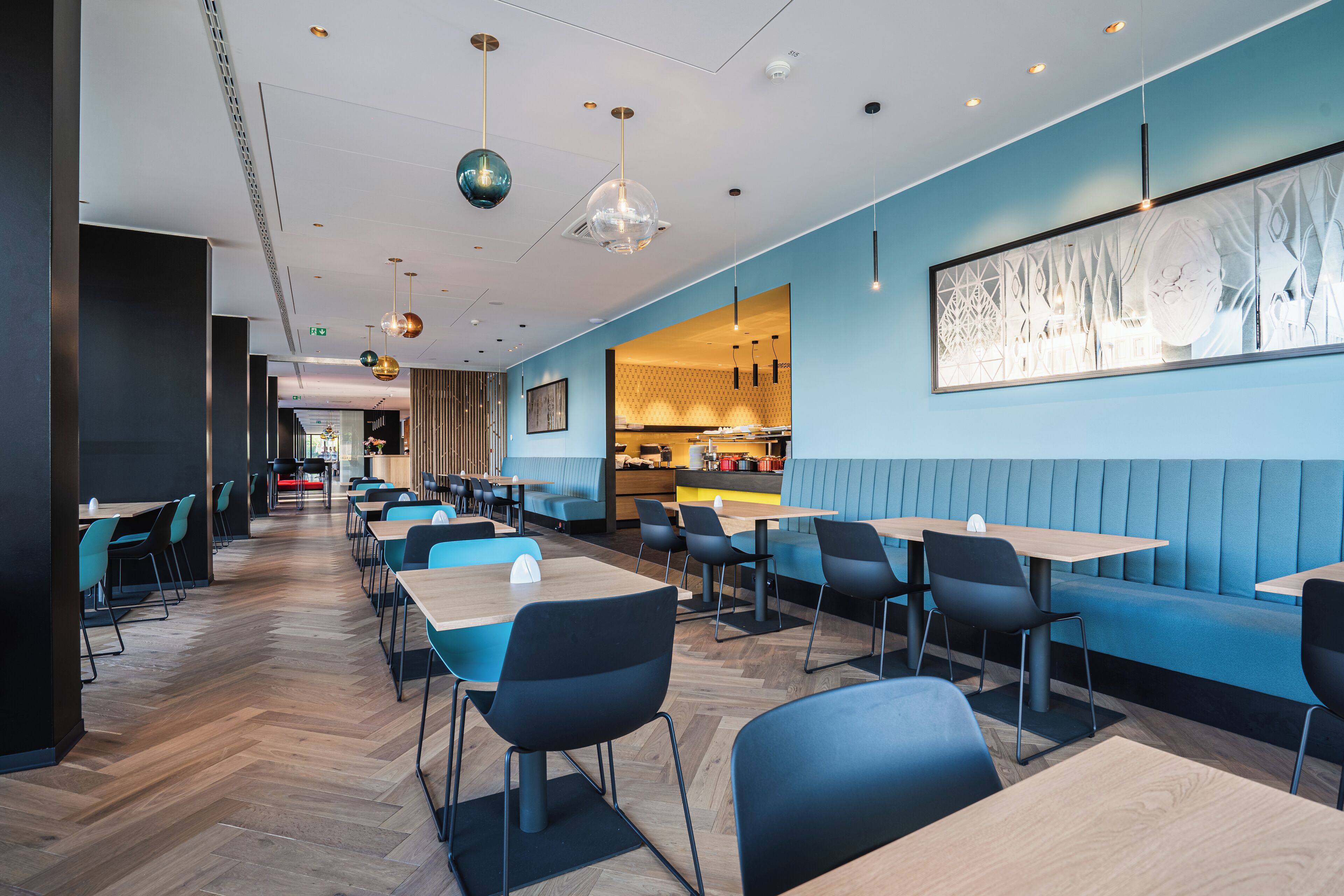 A modern restaurant with blue booths, wooden tables, and black chairs.