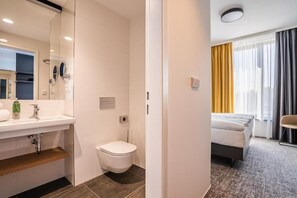 Une chambre d’hôtel avec une salle de bain, un lit et une fenêtre avec des rideaux.