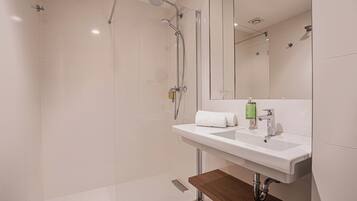 Un baño moderno con cabina de ducha de vidrio, un lavamanos blanco con encimera de madera y un espejo sobre el lavamanos.
