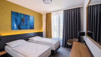 A hotel room with two beds, a desk, a chair, a large mirror, and a painting on the wall.