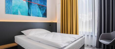 A modern hotel room with a large bed, a nightstand, a chair, and a large abstract painting on the wall.