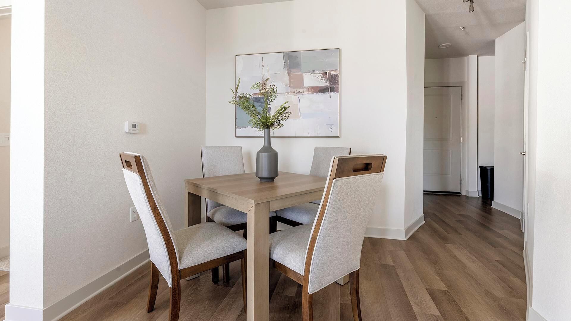 Un coin repas avec une table en bois, quatre chaises rembourrées et un vase agrémenté de plantes vertes.