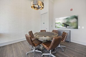 A conference room with a round table, leather chairs, a modern chandelier, a mounted TV, and a door. - Landing | Chic 1BD, Gym, Clubhouse (Nashville)