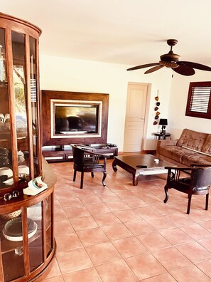 A living room with a television, two armchairs, a coffee table, a cabinet, and a ceiling fan.