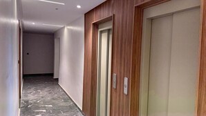 Un couloir avec un mur lambrissé en bois, une porte dotée d’une poignée et un sol en marbre.