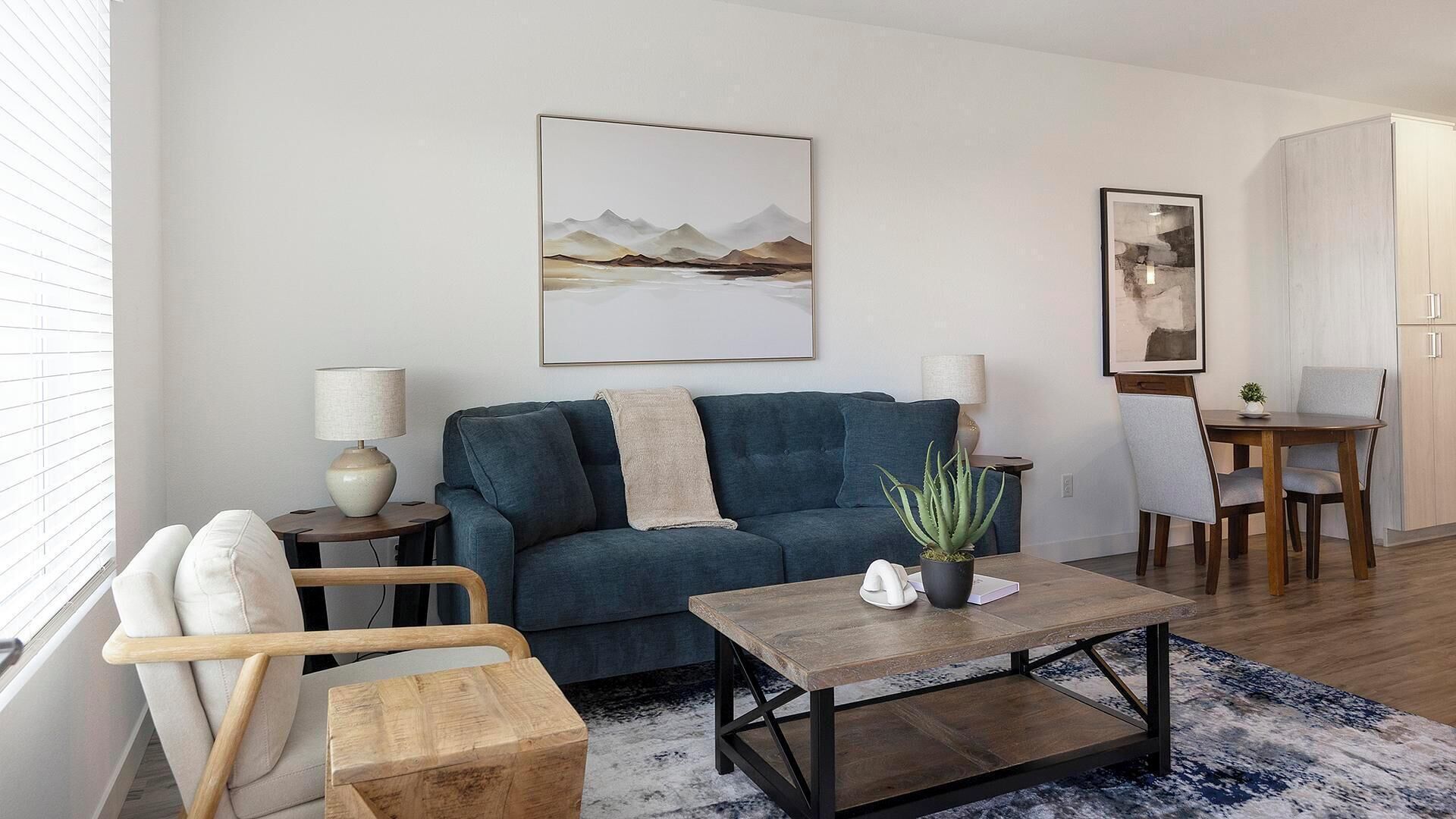 Un salon moderne avec un canapé bleu, une table basse en bois et un coin repas comprenant une table et des chaises.