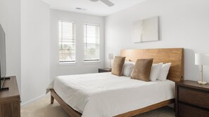 A bedroom with a wooden headboard, a bed with white bedding, two bedside lamps, and a large window with blinds. - Landing | Incredible 1BD, Gym, Clubhouse (Raleigh)