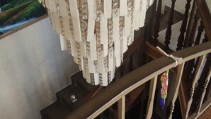 Un lustre aux motifs dorés et blancs, un escalier en bois et un tableau encadré au mur.