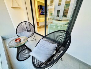 Ein Balkon mit zwei schwarzen Korbstühlen und einem kleinen Glastisch, mit Blick auf die Stadtlandschaft.