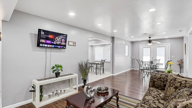 A spacious living room with a flat-screen TV mounted on the wall, a wooden coffee table, a patterned sofa, and a dining area with chairs and a table. - Casa Zen Retreat •Great Backyard• Near I-10 & Loop (El Paso)