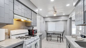 A compact kitchen with a gas stove, microwave, and a dining table with chairs. - Casa Zen Retreat •Great Backyard• Near I-10 & Loop (El Paso)