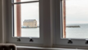 Blick durch zwei Fenster eines Gebäudes auf ein Gewässer, im Hintergrund ein Steg.