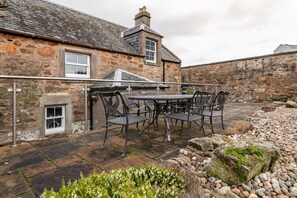 A stone building with a tiled patio, outdoor seating, and a small window. - Burnside, The Toft | Elie (Elie)