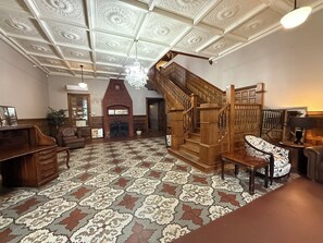 A spacious room with a patterned floor, a fireplace, a wooden staircase, and a chandelier.
