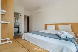 A hotel room with a bed, a wooden headboard, a white wall, and an air conditioning unit. - Apt w/ Barbecue 650m From the Lagoon Ruh0109 (Florianópolis)