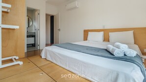 A hotel room with a bed, a wooden headboard, a white wall, and an air conditioning unit. - Apt w/ Barbecue 650m From the Lagoon Ruh0109 (Florianópolis)