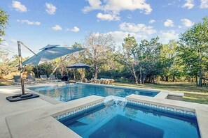 A swimming pool with lounge chairs and umbrellas, surrounded by trees.