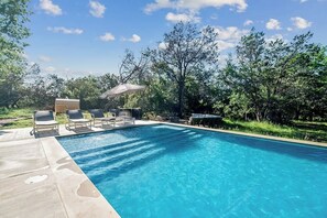 A rectangular swimming pool with clear blue water, surrounded by a concrete deck. There are lounge chairs and a covered seating area with a table and umbrella. - Suniland w/Pool, Hot-tub and sauna! (Fredericksburg)